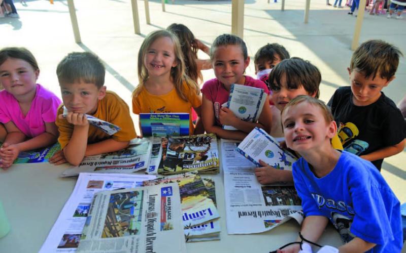 Students surround the table Friday at Taylor Creek Elementary School’s Career Day to learn what it takes to become a journalist. ERICK MITHCELL | DISPATCH RECORD