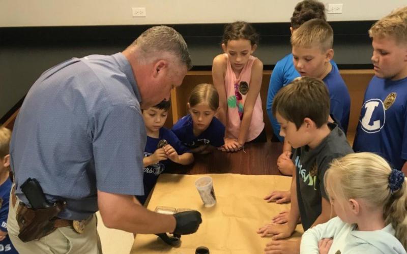 Lampasas Police Department Lt. Investigator Charlie Boswell lifts fingerprints from a cup as College for Kids participants watch. His investigation was part of a Junior Police Academy offering. LAMPASAS POLICE DEPARTMENT FACEBOOK