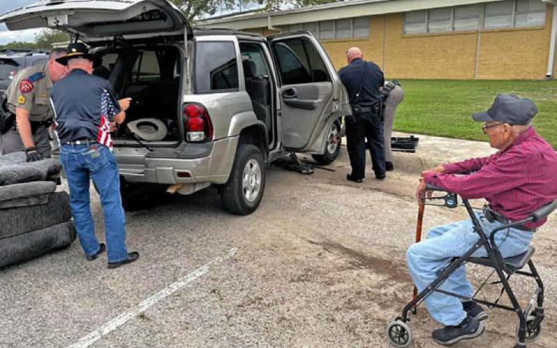 Law enforcement officers Sgt. Ryan McKittrick, Trooper Dennis Jones, School Resource Officer Dustin Roscoe and another volunteer help change a tire for World War II veteran Lupe Dimas, at right, after a program at Lampasas Middle School last week. courtesy photo | jera freeman
