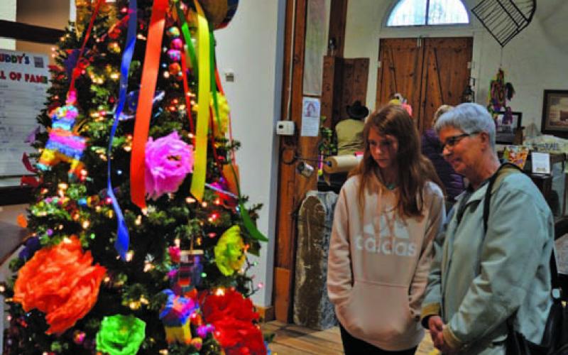 Taylor Jabara, at left, and Chris Clark look at the Christmas trees on display at the Lampasas County Museum during Saturday’s Carol of Lights festivities. ERICK MITCHELL | DISPATCH RECORD