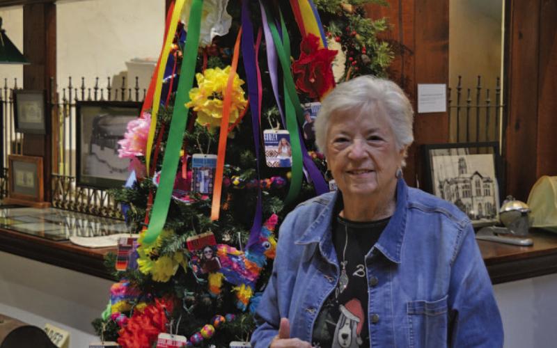 Carol Wright stands by the Aggie Moms decorated Christmas tree at the Lampasas County Museum. She won’t be at the museum Saturday night during Carol of Lights, but instead she will be serving as grand marshal for the Holidazzle Christmas Parade. ERICK MITCHELL | DISPATCH RECORD