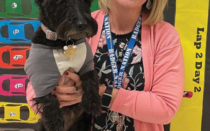 Taylor Creek Principal Shona Moore holds school dog Nessy as she stands in front of a paper racetrack. Every class at each grade level has a car on the track. Classes that have perfect attendance move to the finish line to obtain a Coke float as a reward. erick mitchell | dispatch record