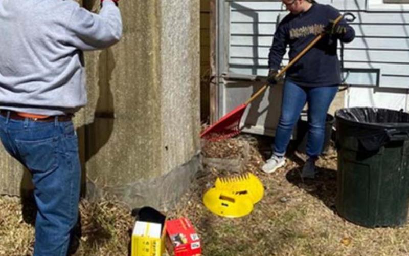 A student rakes leaves from inside Mary Tittle’s greenhouse, while an adult volunteer works on repairing the roof. COURTESY PHOTO