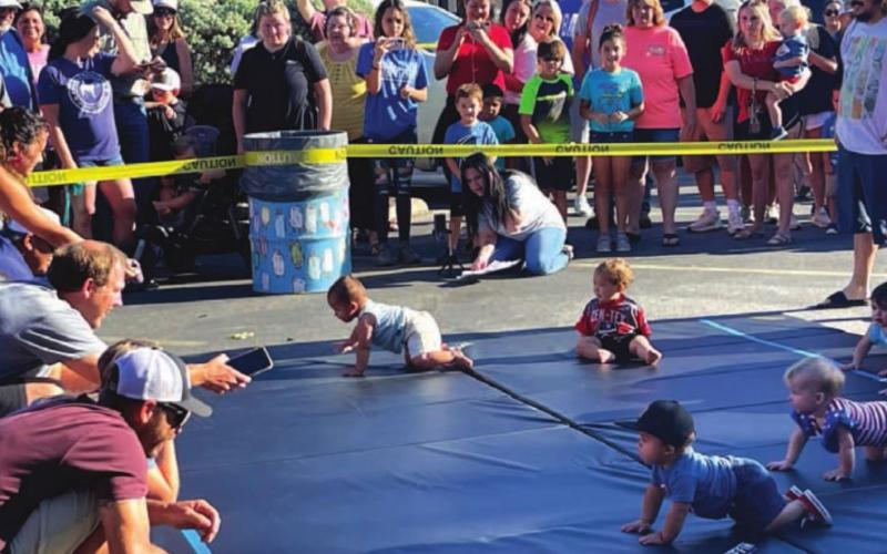 Parents encourage their child to cross the mat, using apples, phones and even keys as enticement during the annual Spring Ho Diaper Derby. MASON HINES | DISPATCH RECORD