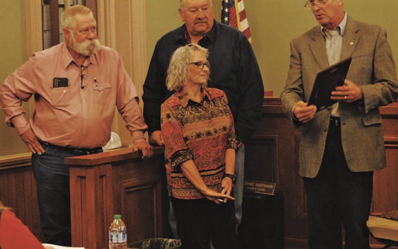 The Lampasas County Commissioners Court presented retiring County Clerk Connie Hartmann with a plaque to recognize her service over the last four decades. Standing behind Hartmann are Precinct 3 Commissioner Lewis Bridges, at left, and Precinct 4 Mark Rainwater as County Judge Randy Hoyer, at right, reads from Hartmann’s plaque. HUNTER KING | DISPATCH RECORD