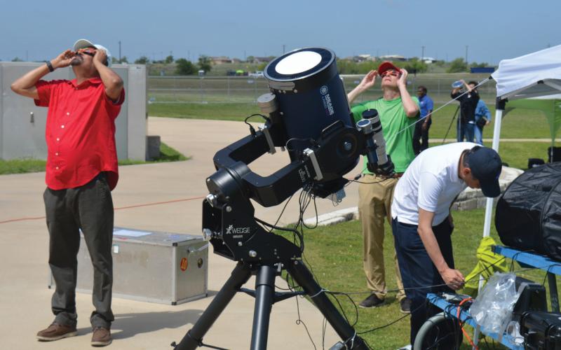 At left, NASA’s Dr. Natchimuthuk Gopalswamy views the partial phase of the eclipse through solar glasses along with other members participating in NASA’s research station set up at the 580 Sports Park on Monday. ERICK MITCHELL | DISPATCH RECORD
