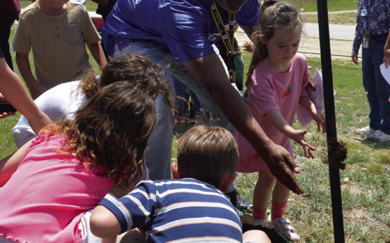 Taylor Creek Elementary School Principal Mark Sheppard assists students in pouring dirt to help plant the new tree on campus. ERICK MITCHELL | DISPATCH RECORD