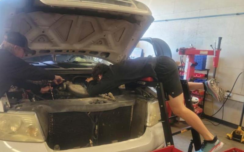 Nathan Abken, at right, leans over the hood of a pickup as he works on an engine as part of his training this spring in the Lampasas High School Auto Tech II class. FILE PHOTO
