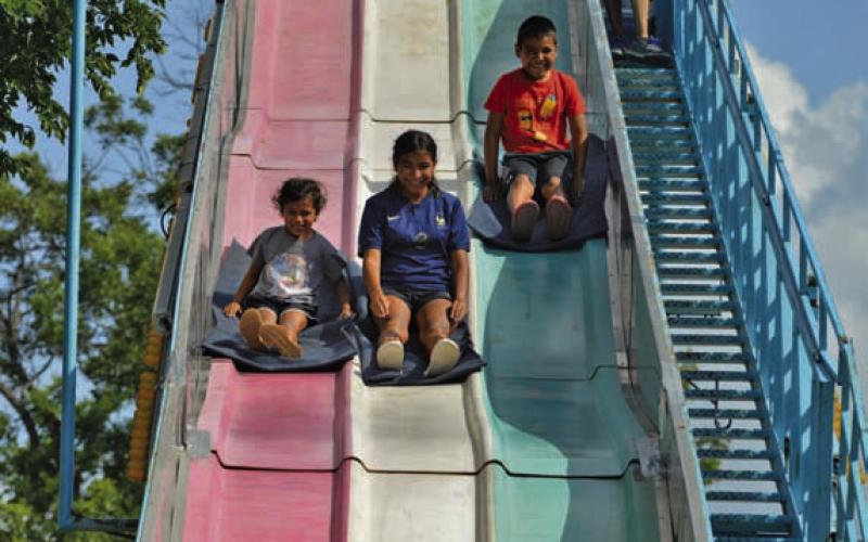 From left, Lupita, Mireya and Andrew Rodriguez race down the slide at Spring Ho’s carnival within W.M. Brook Park. ERICK MITCHELL | DISPATCH RECORD