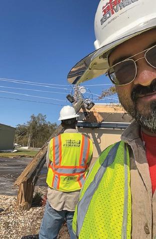 Armando Rosales poses for a work selfie that includes in the background a broken power pole caused by heavy winds from Hurricane Helene in Georgia. Rosales spent more than a month on the job assisting in restoration efforts after Hurricanes Helene and Milton struck the Southeast earlier this year. courtesy photo