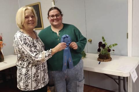 Holly Hines, at right, garnered the Best in Show Award for her arrangement using dark-purple ranunculus. Sheri Stone presented the award on behalf of the L-M Garden and Civic Club. COURTESY PHOT0