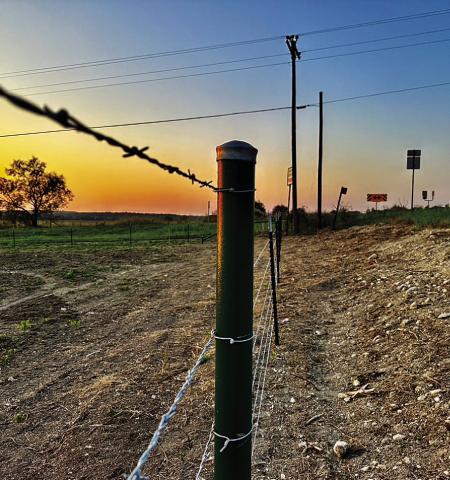 As the sun rises over Lampasas County, a new fence surrounds a vast hayfield, standing strong against the morning light. The sturdy metal posts and taut wire symbolize the resilience and determination of the agricultural community to rebuild JOYCESARAH MCCABE | DISPATCH RECORD