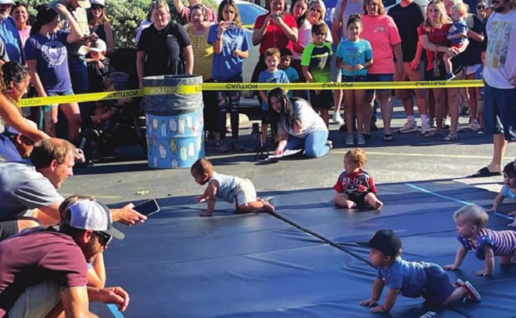 Parents encourage their child to cross the mat, using apples, phones and even keys as enticement during the annual Spring Ho Diaper Derby. MASON HINES | DISPATCH RECORD
