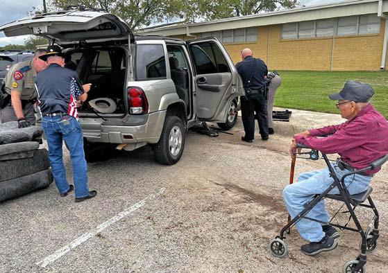 Law enforcement officers Sgt. Ryan McKittrick, Trooper Dennis Jones, School Resource Officer Dustin Roscoe and another volunteer help change a tire for World War II veteran Lupe Dimas, at right, after a program at Lampasas Middle School last week. courtesy photo | jera freeman