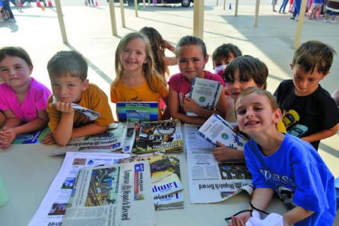 Students surround the table Friday at Taylor Creek Elementary School’s Career Day to learn what it takes to become a journalist. ERICK MITHCELL | DISPATCH RECORD