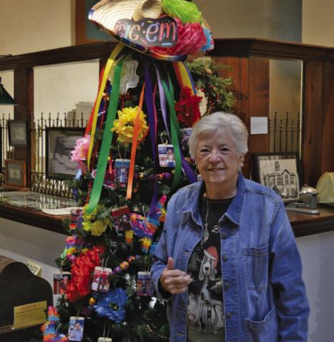 Carol Wright stands by the Aggie Moms decorated Christmas tree at the Lampasas County Museum. She won’t be at the museum Saturday night during Carol of Lights, but instead she will be serving as grand marshal for the Holidazzle Christmas Parade. ERICK MITCHELL | DISPATCH RECORD