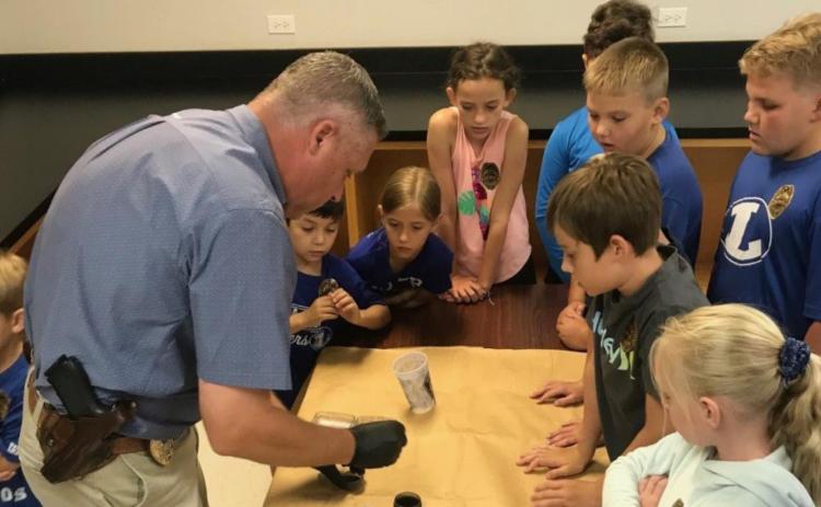 Lampasas Police Department Lt. Investigator Charlie Boswell lifts fingerprints from a cup as College for Kids participants watch. His investigation was part of a Junior Police Academy offering. LAMPASAS POLICE DEPARTMENT FACEBOOK