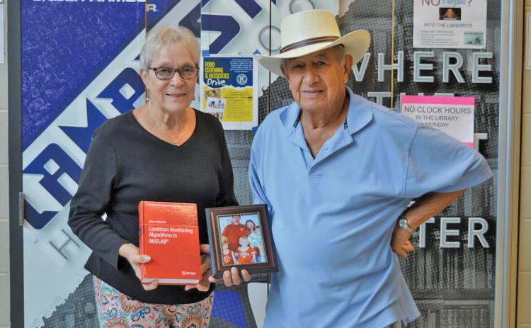erick mitchell | dispatch record Sherry and Bob Ellis hold a photo of Adam Jablonski’s family and the former LHS exchange student’s published textbook. Jablonski is a university professor now in Poland.