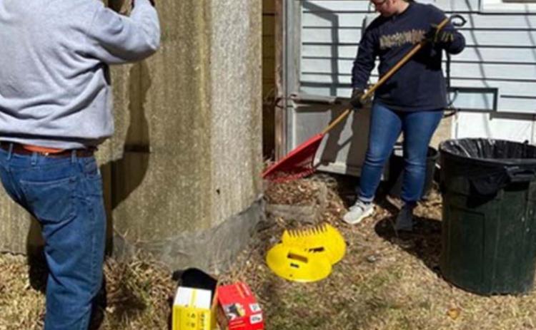 A student rakes leaves from inside Mary Tittle’s greenhouse, while an adult volunteer works on repairing the roof. COURTESY PHOTO