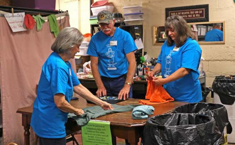 joycesarah mccabe | dispatch record Billy James and Marilyn James stand on one side of the clothing sorting table folding T-shirts, while Frieda Gayheart stands on the other side and assists.