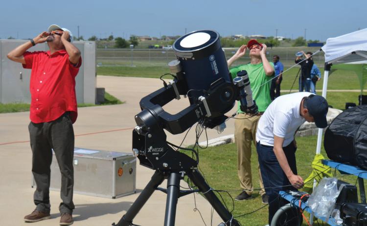 At left, NASA’s Dr. Natchimuthuk Gopalswamy views the partial phase of the eclipse through solar glasses along with other members participating in NASA’s research station set up at the 580 Sports Park on Monday. ERICK MITCHELL | DISPATCH RECORD